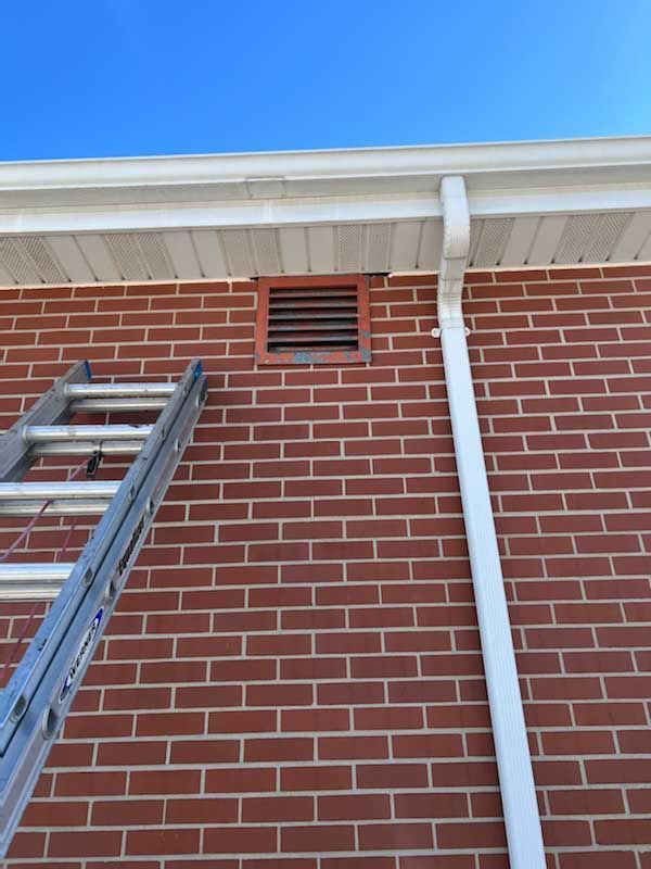 Ladder against red brick wall beneath white roof trim and downspout