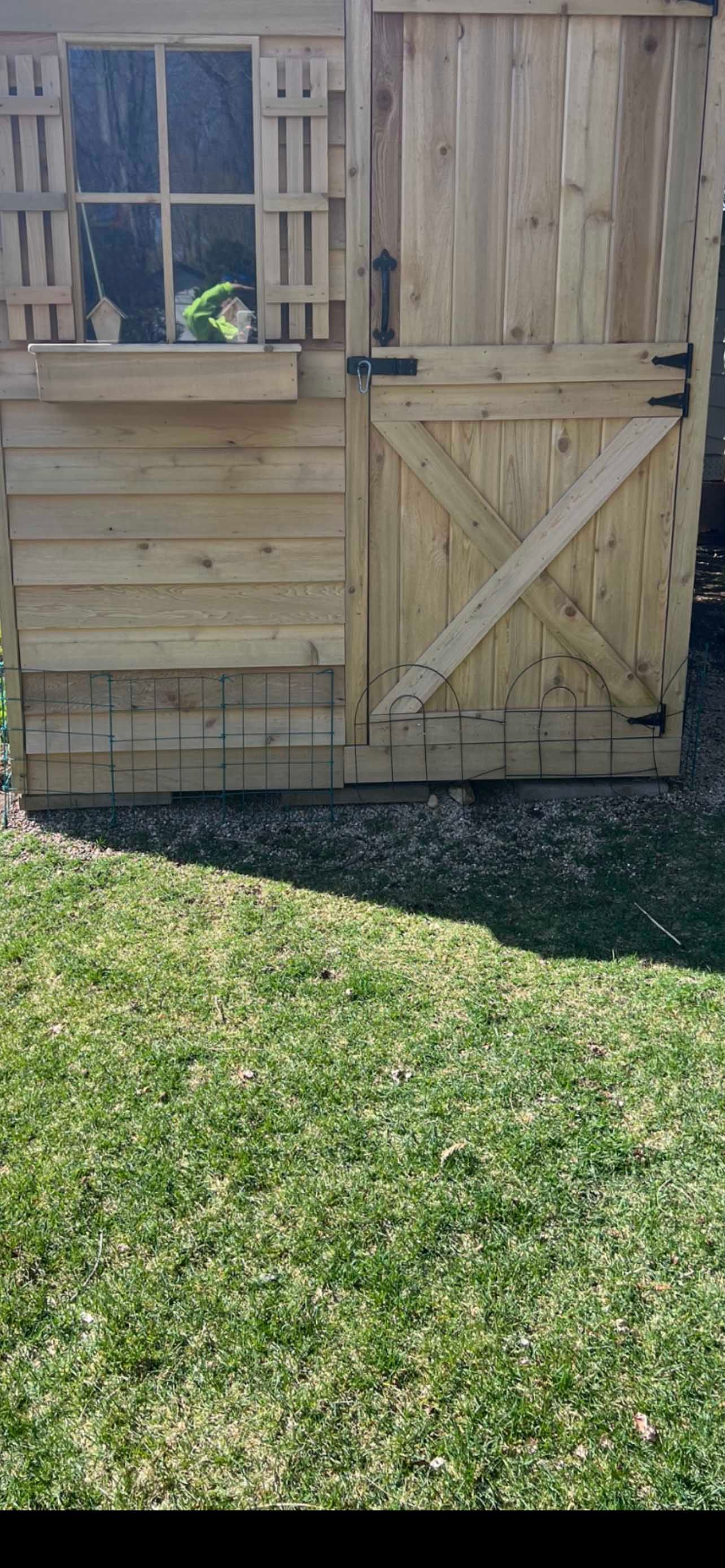 Wooden garden shed with a small window, door, and grassy lawn in front.