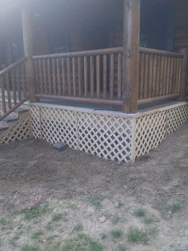 Wooden porch with railing and white lattice skirting on a dirt yard.