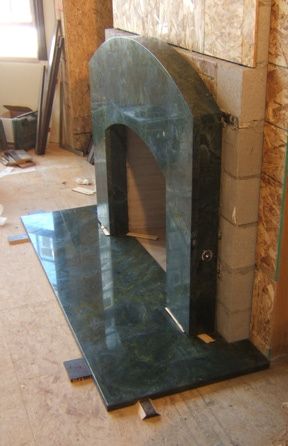 A green marble fireplace is being built in a living room.