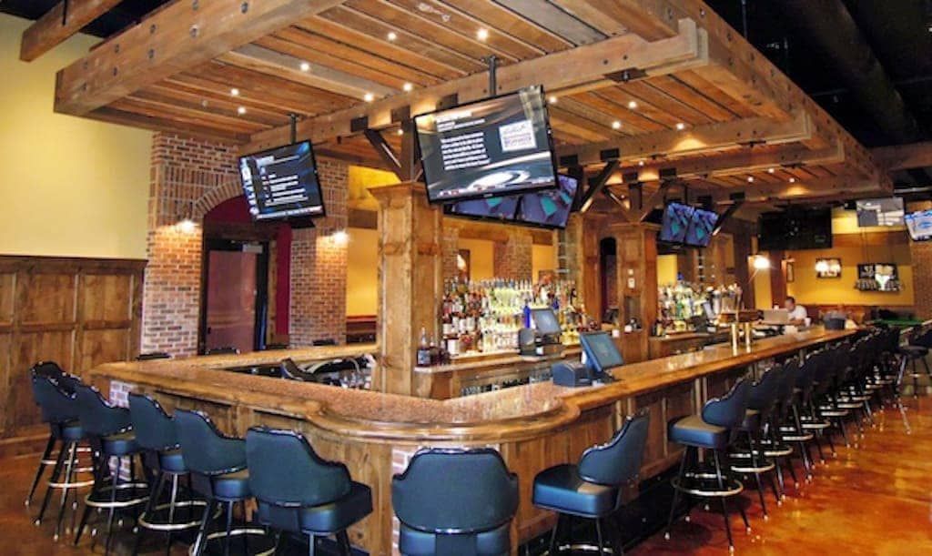 A long bar in a restaurant with televisions hanging from the ceiling