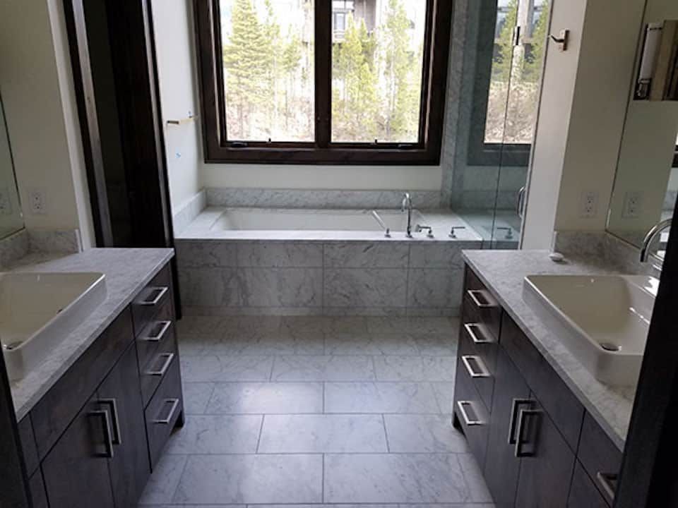 A bathroom with two sinks , a tub and a window.