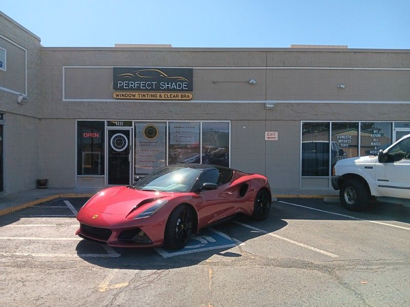 A red sports car is parked in front of a building that says perfect shade
