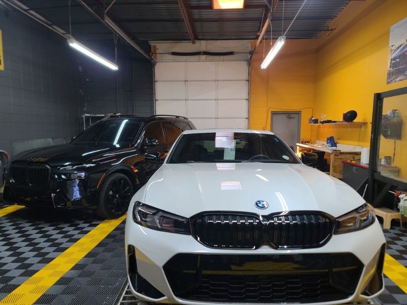 A white car is parked in a garage next to a black car.
