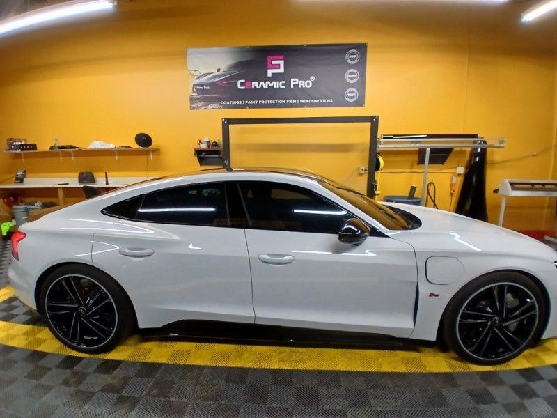 A white car is parked in a garage with a yellow wall behind it.