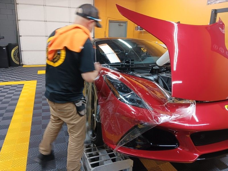 A man is working on a red sports car with the hood open