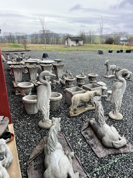 Outdoor display of concrete garden statues and planters on gravel.