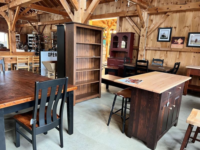 Furniture showroom featuring wood tables, chairs, and shelving units. Rustic decor in a barn-like setting.