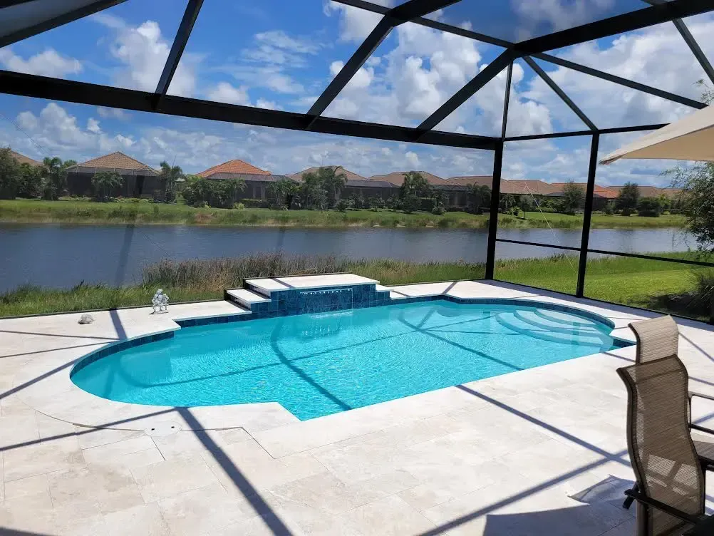 A large swimming pool is surrounded by a screened in area with chairs and umbrellas