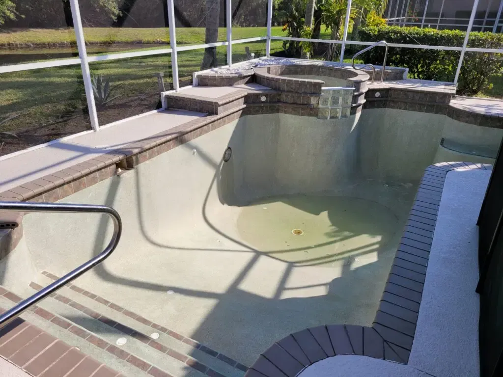 An empty swimming pool with a hot tub in the background