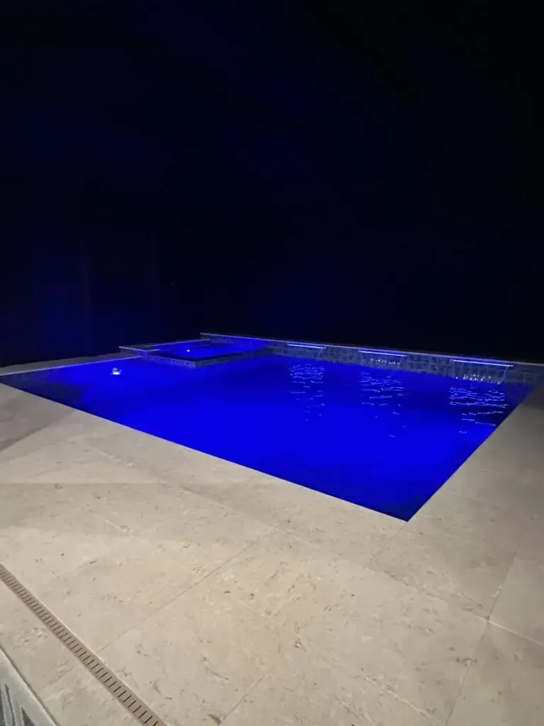 A large swimming pool is lit up at night with blue lights
