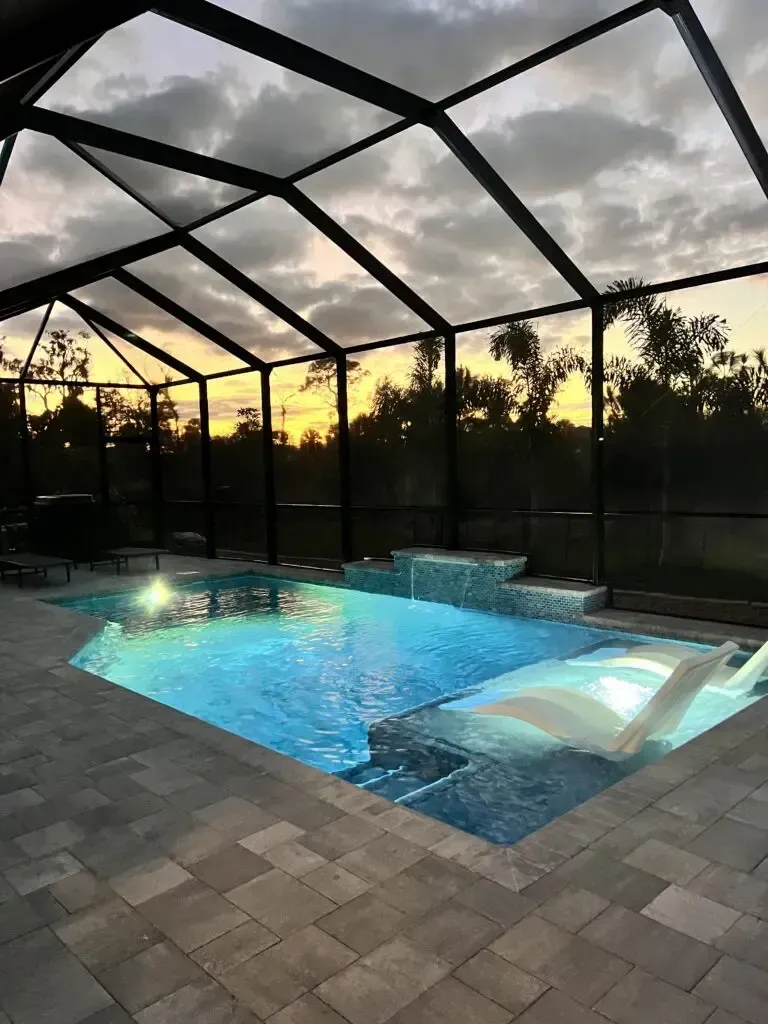 A large swimming pool with a screened in area at sunset