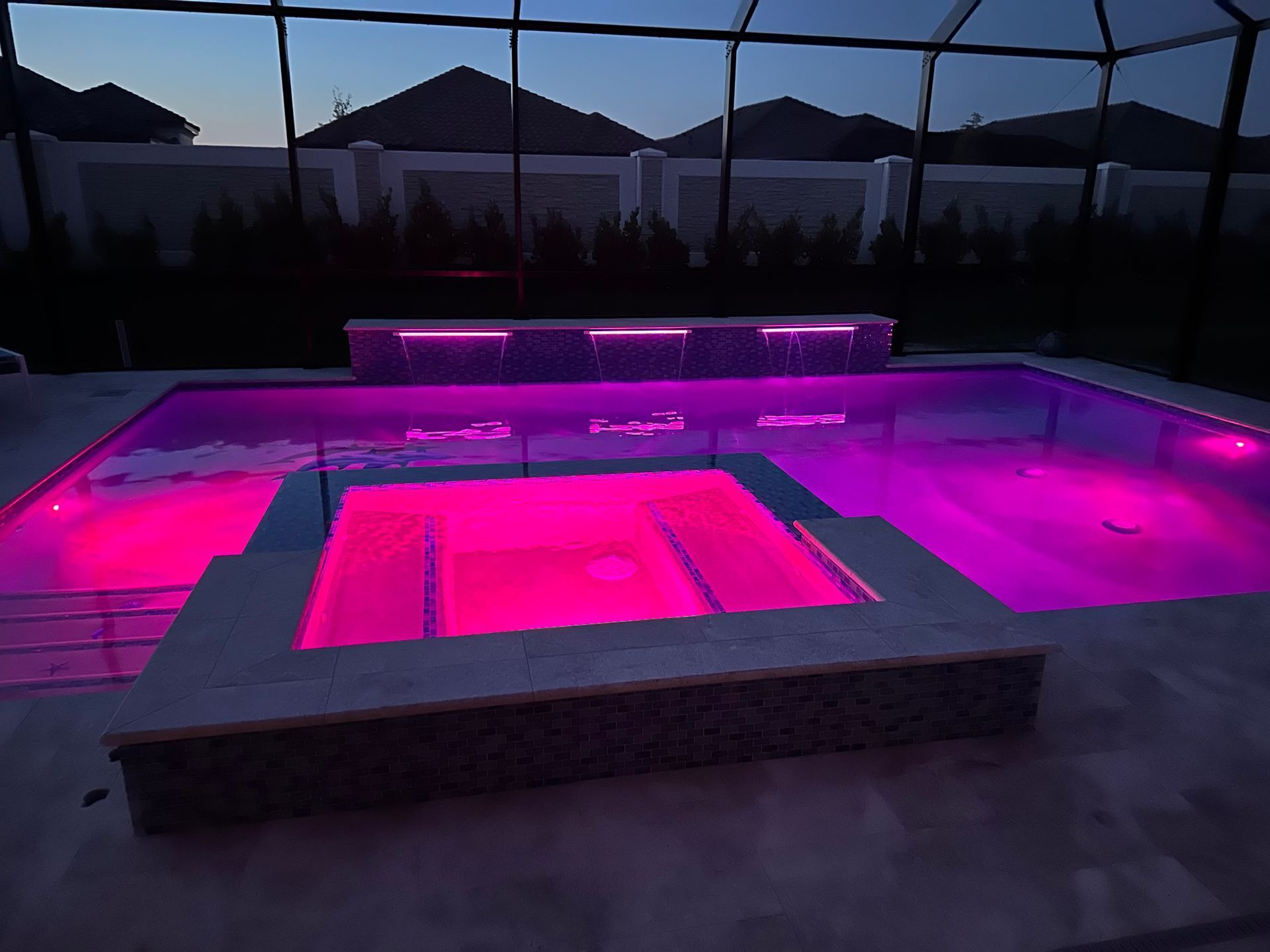 A large swimming pool is lit up with pink lights at night.