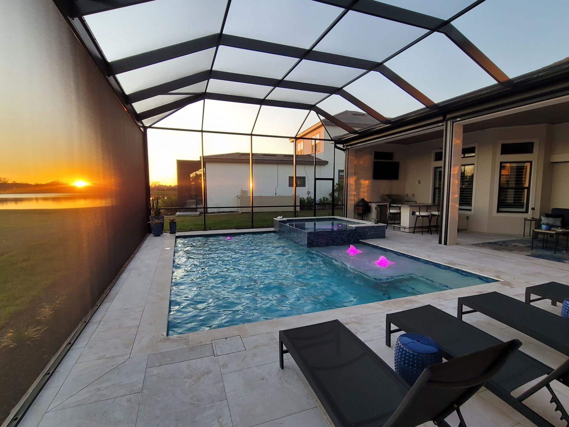 A large swimming pool with a screened in area and a sunset in the background