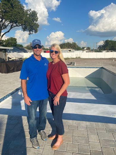 Two people in blue and maroon shirts are standing next to each other in front of a construction site