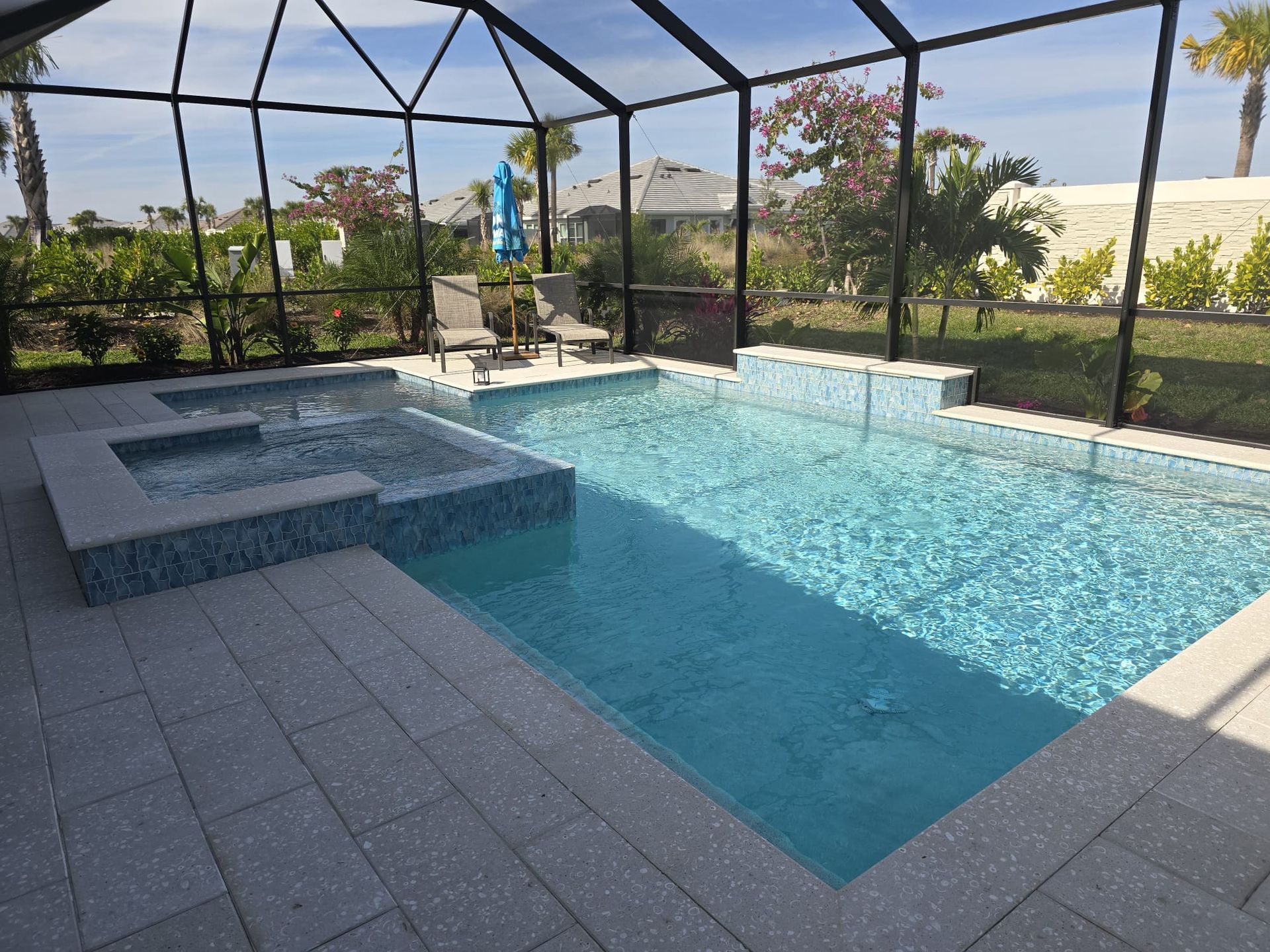 A screened-in patio featuring a rectangular swimming pool, a square spa, and grey pavers on a sunny day.