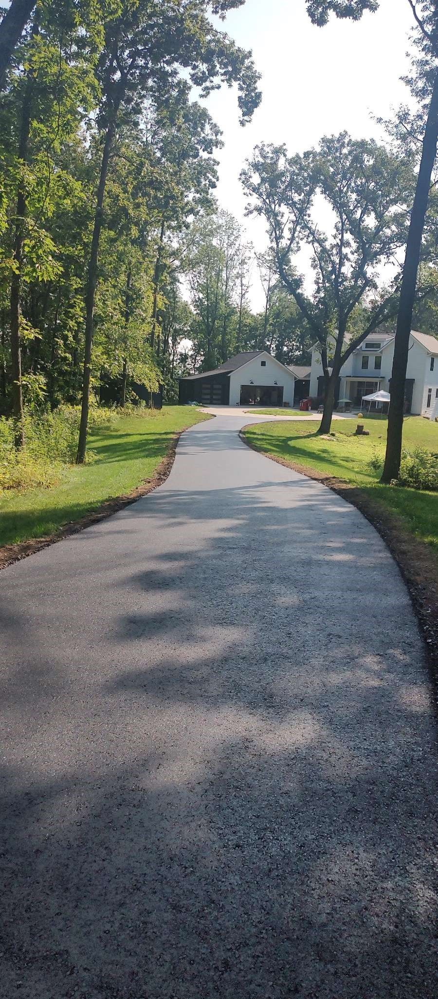 A driveway leading to a house surrounded by trees and grass.