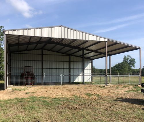 Open-sided metal barn with a white roof in a grassy rural field under a blue sky