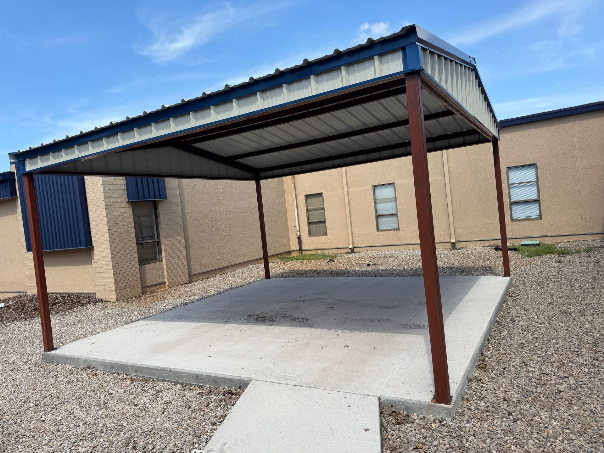 Covered concrete patio with a metal canopy beside a beige building