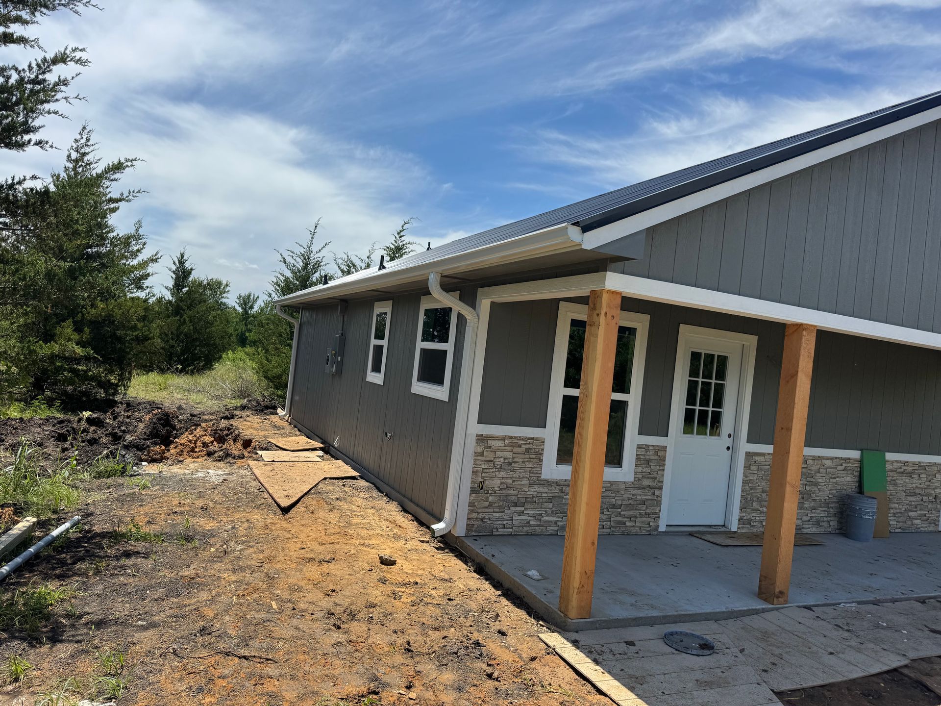 Partially built gray house exterior with white trim and a covered porch under a blue sky