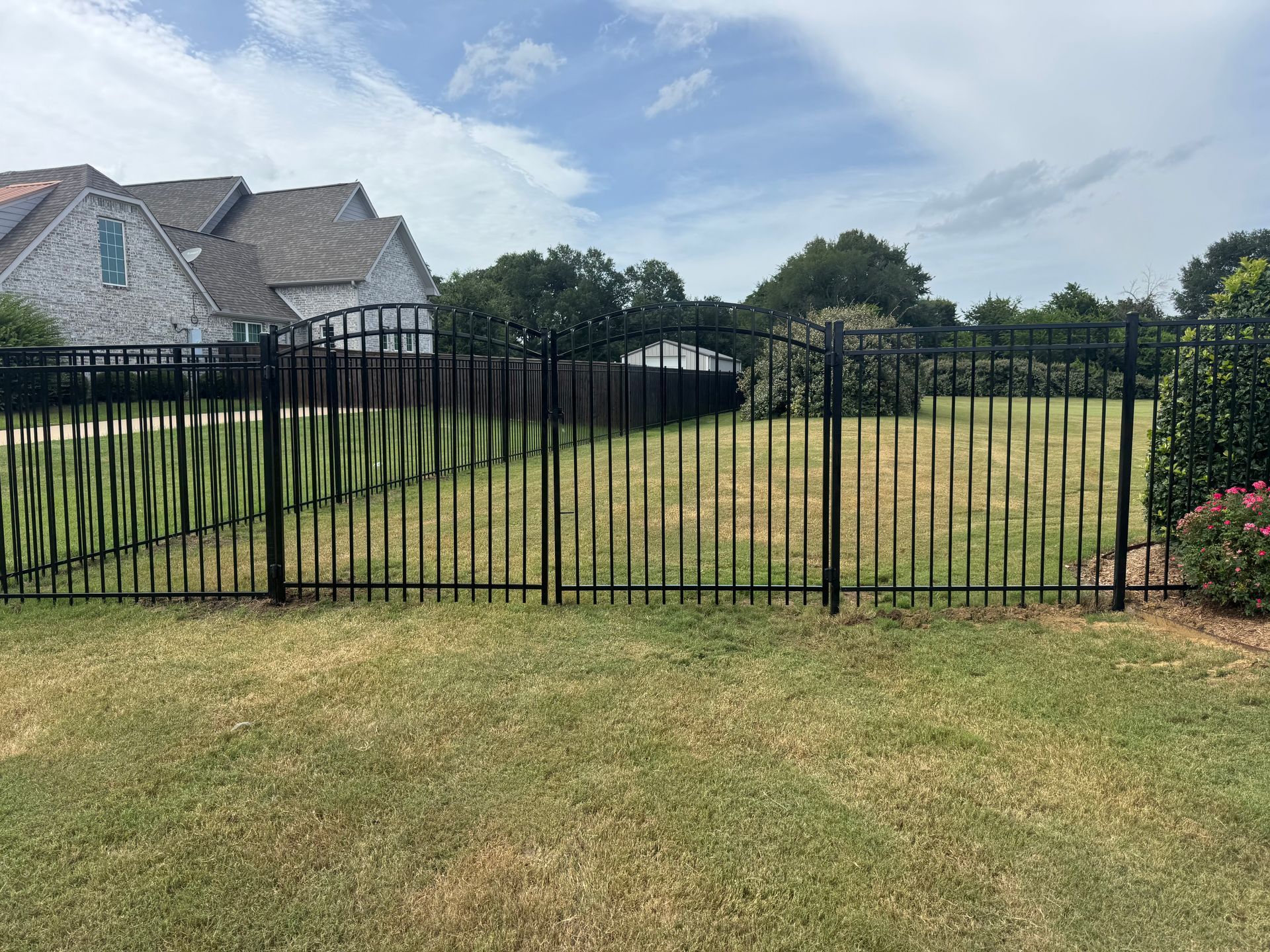 Black metal fence around a grassy yard with houses and trees in the background