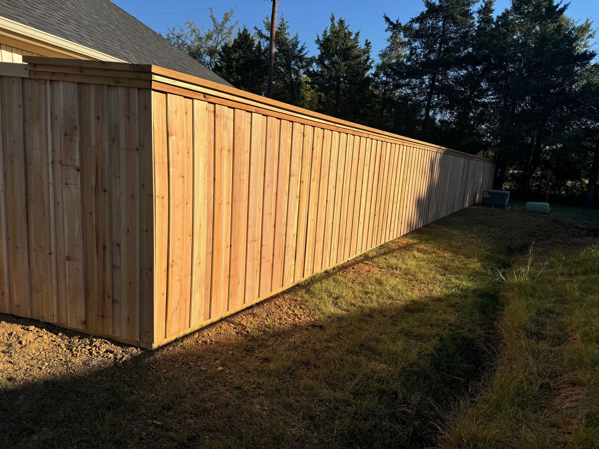 Wooden privacy fence along a grassy yard, lit by sunlight with trees in the background