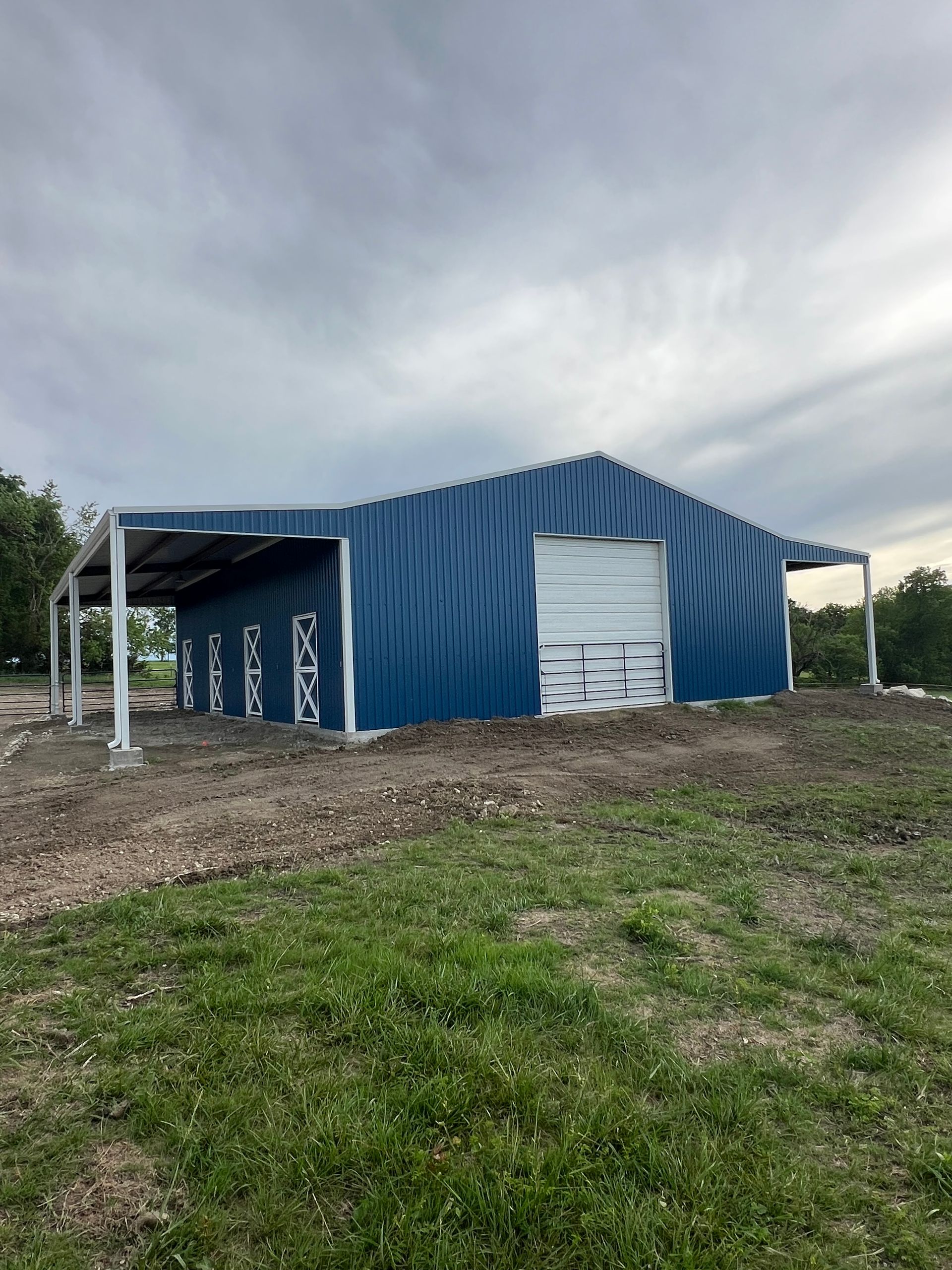 Blue metal shed with white doors on a grassy lot under a cloudy sky