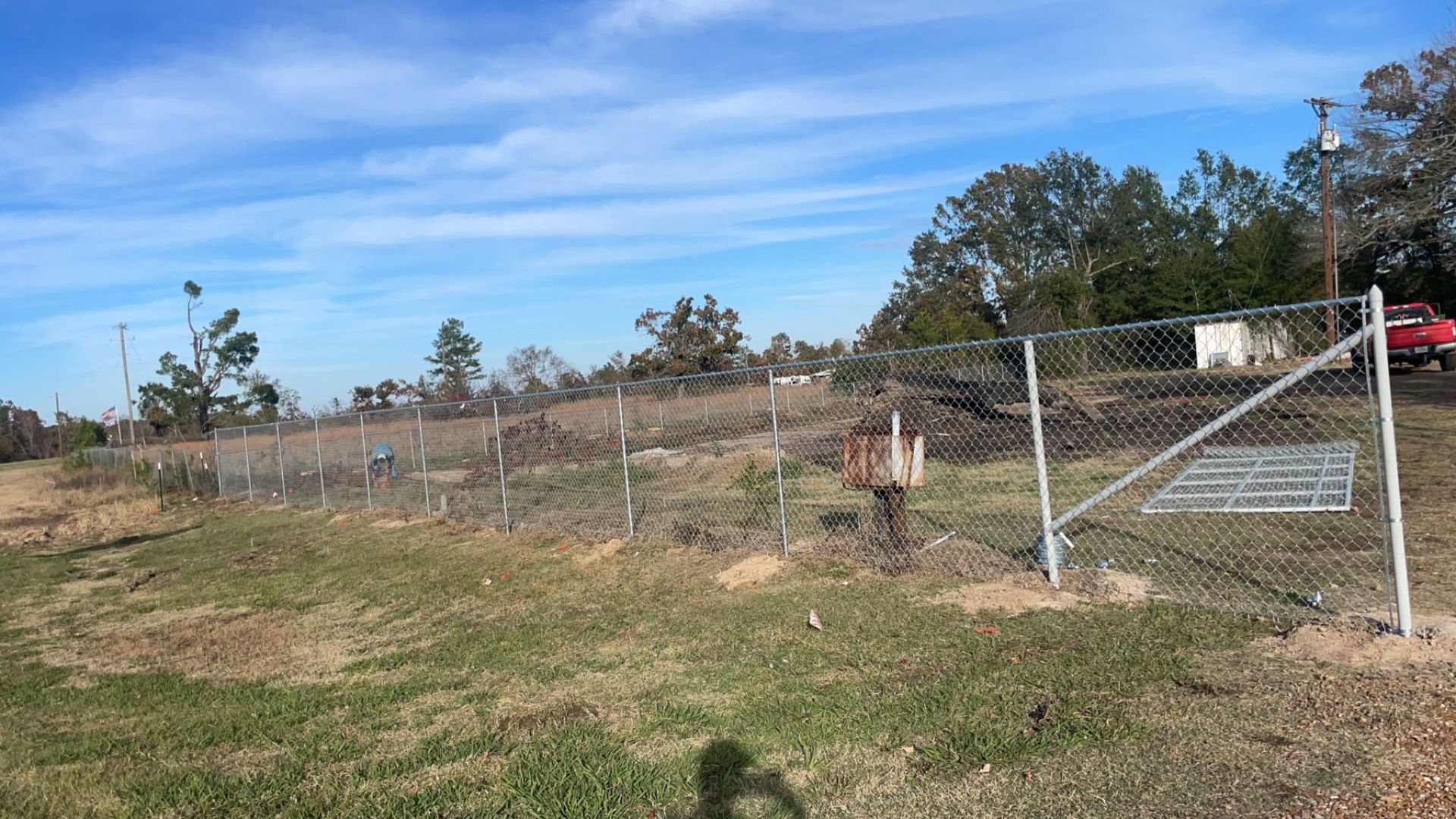 Rural fenced property with a metal gate, dry grass, and a small shed under a clear blue sky
