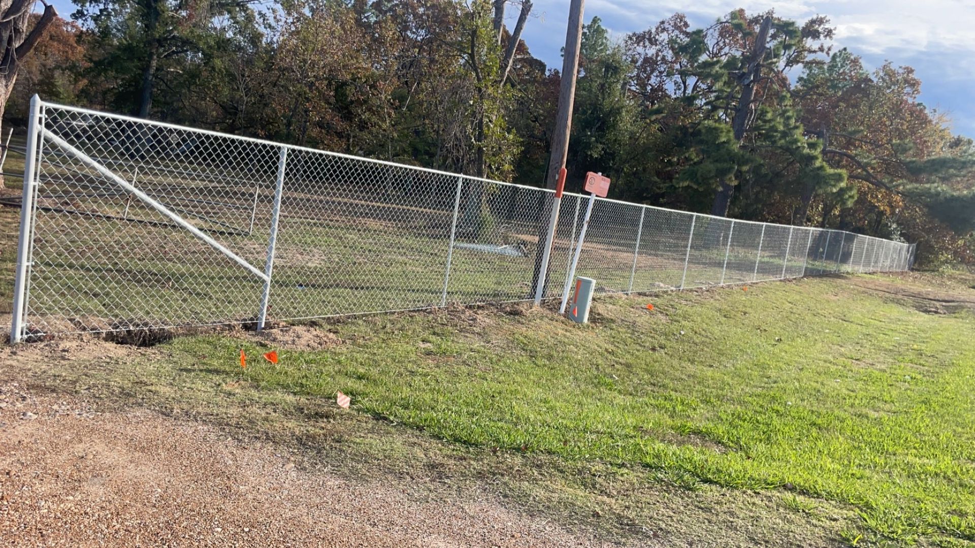 Chain-link fence along a grassy roadside with trees in the background