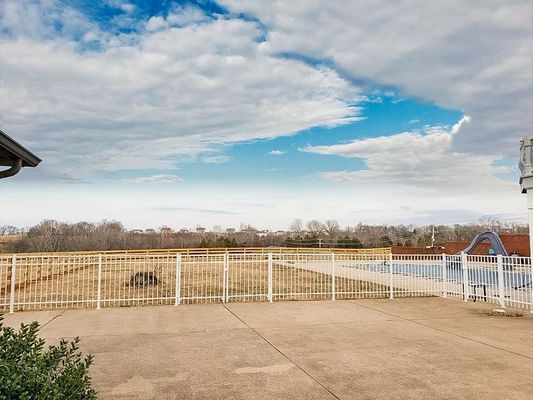A patio with a fence and a swimming pool in the background.