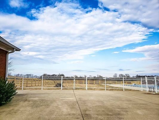 A brick house with a white fence around it and a swimming pool in the background.