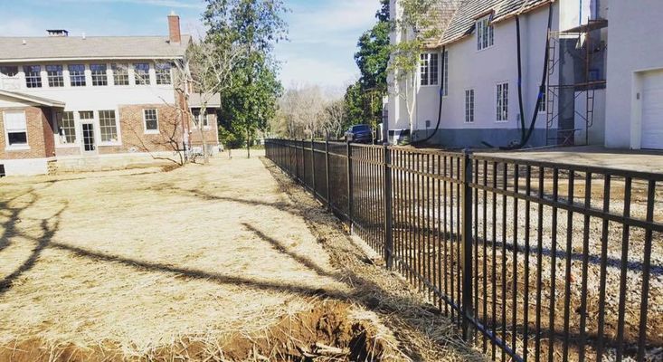 A metal fence is surrounding a dirt field in front of a house.