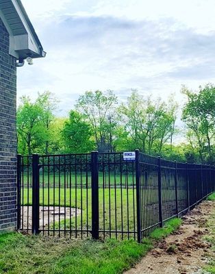 A black fence surrounds a lush green field next to a brick building.