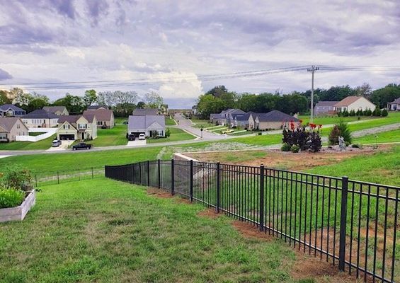 A black fence surrounds a lush green field in a residential area.