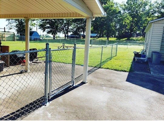 A chain link fence surrounds a patio with a white house in the background