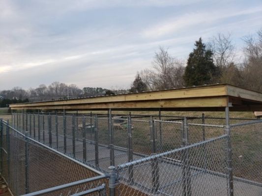 A chain link fence surrounds a large wooden structure in a field.