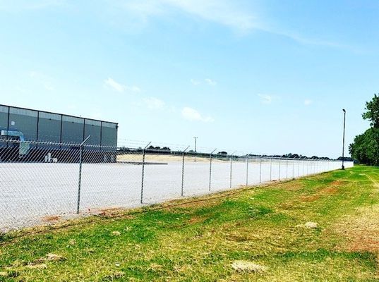 A chain link fence surrounds a grassy field in front of a large building.