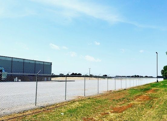 A chain link fence surrounds a parking lot with a large building in the background.