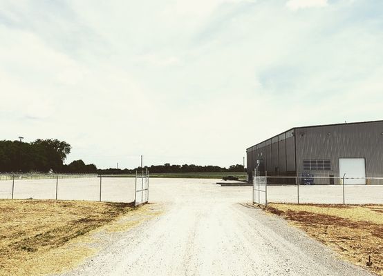 A dirt road leading to a large building with a fence around it.