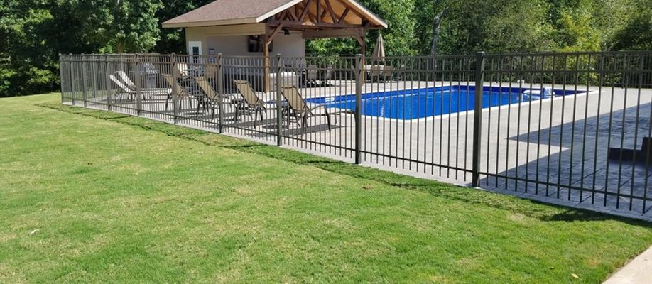 A fence surrounds a swimming pool with a gazebo in the background.