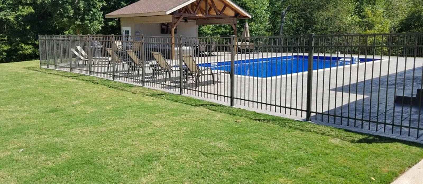 A fence surrounds a swimming pool with a gazebo in the background.