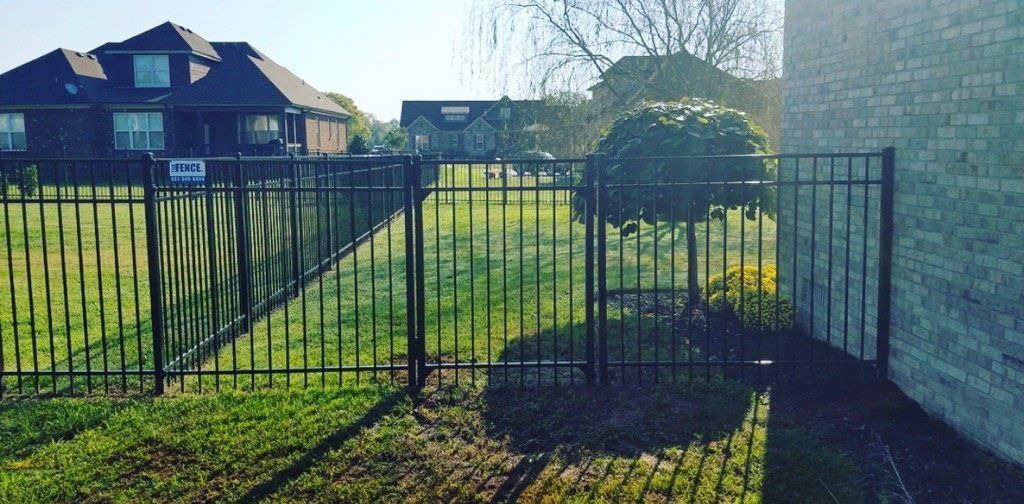 A black metal fence surrounds a lush green yard in front of a house.