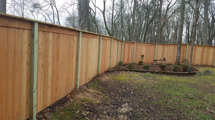 A wooden fence in a backyard with trees in the background.