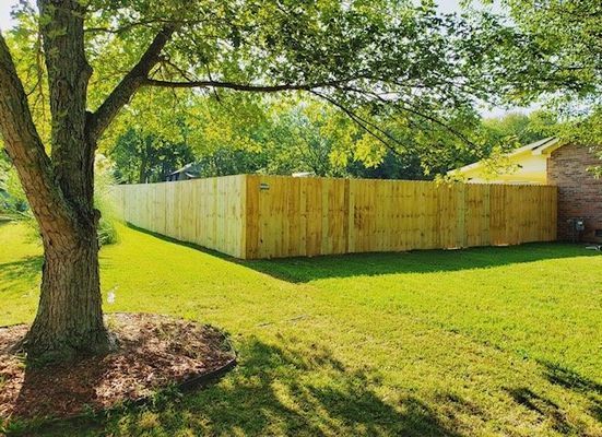 A wooden fence is in the middle of a lush green yard next to a tree.