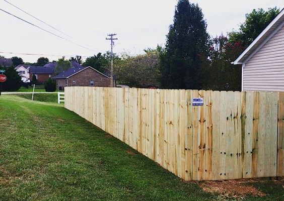A wooden fence surrounds a lush green yard next to a house.