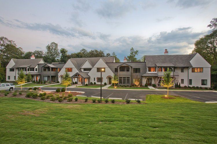 Multi-unit residential building with gray and white exterior, trees, and grassy lawn.