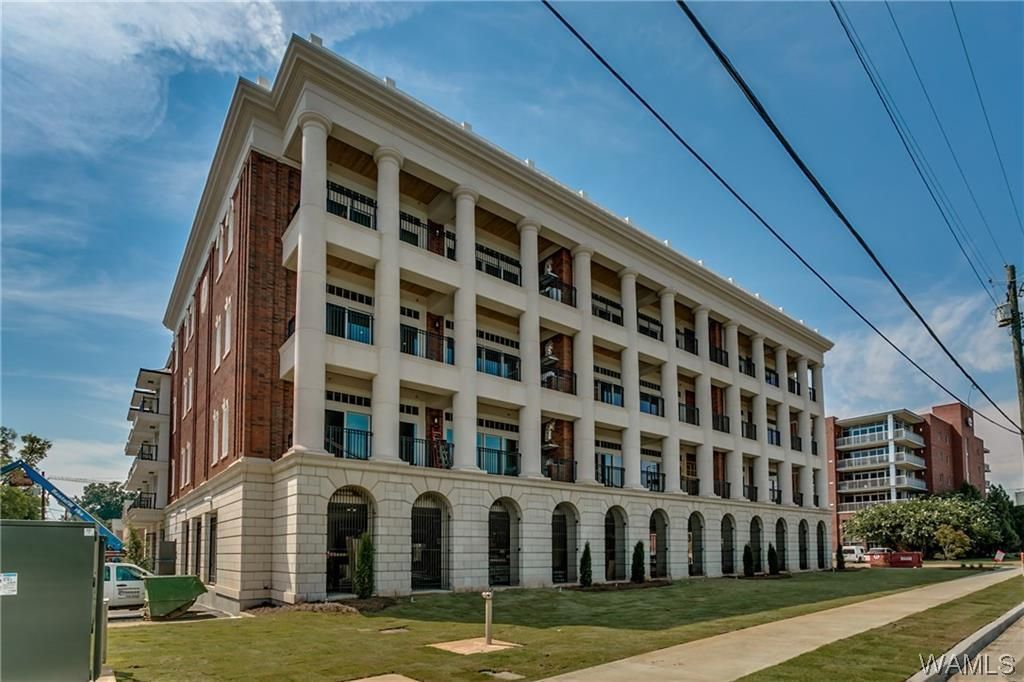 Multi-story brick and white building with arched ground floor and balconies, under a blue sky.
