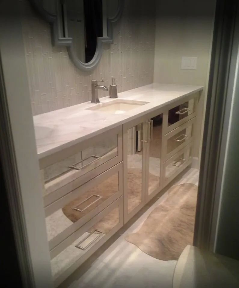 Bathroom vanity with mirrored cabinet doors, a countertop, and a decorative mirror above the sink.