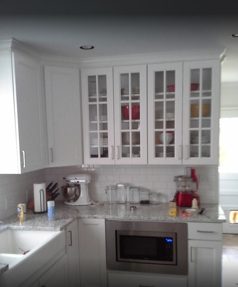 White kitchen cabinets, countertop, and appliances. Microwave built-in below glass-fronted cabinets.