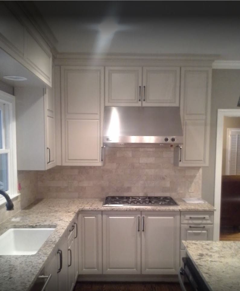 Cream-colored kitchen cabinets with granite countertops, stainless steel range hood, and tile backsplash.